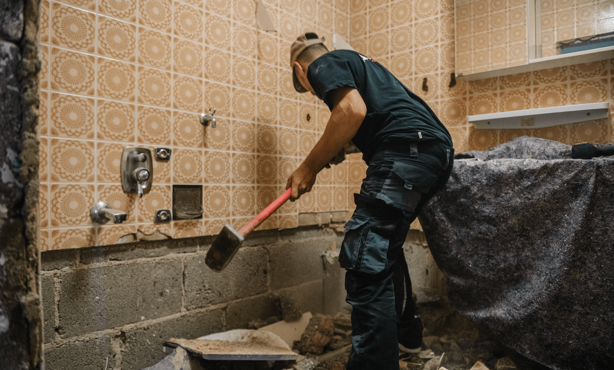 Worker swings sledge hammer to demolish bathroom for home remodel