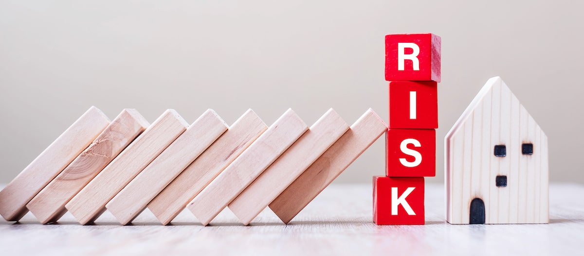 Wooden blocks are leaning toward a small house and a stack of blocks that spell out 'risk'.