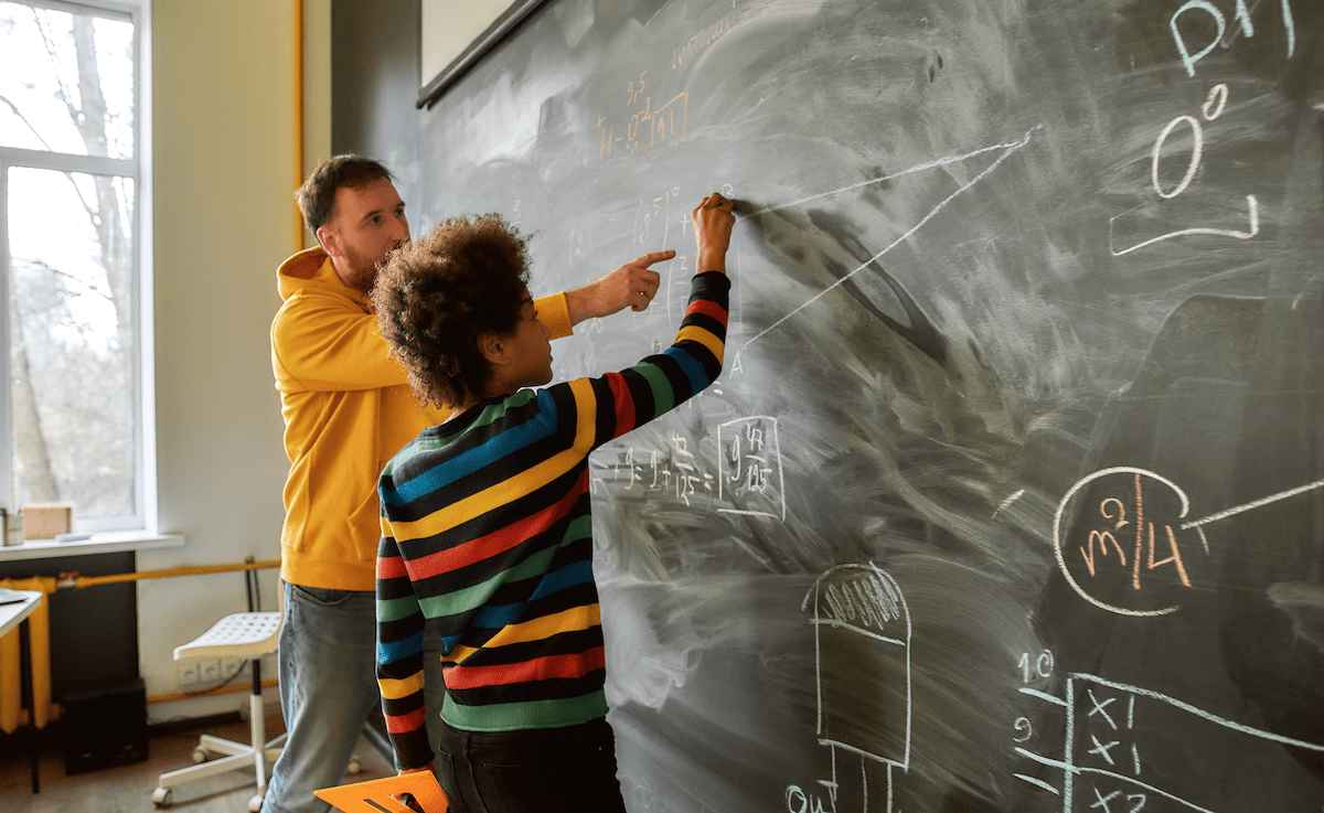 Teacher at blackboard doing math with student