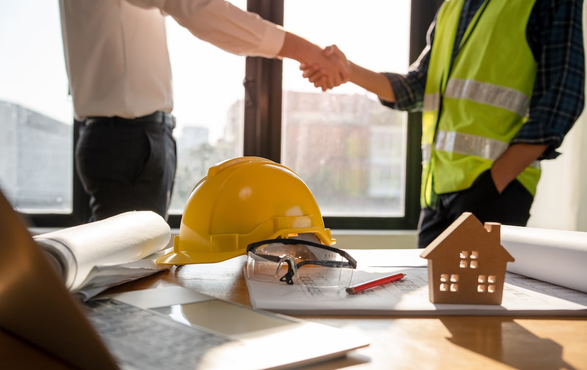 Builder shaking hands with businessman in front of office desk
