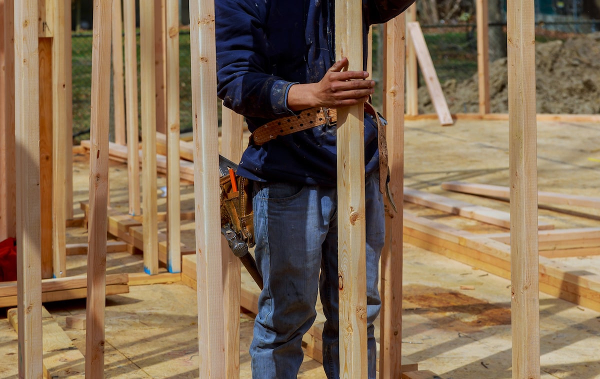 Carpenter holds wood framing member in house under construction