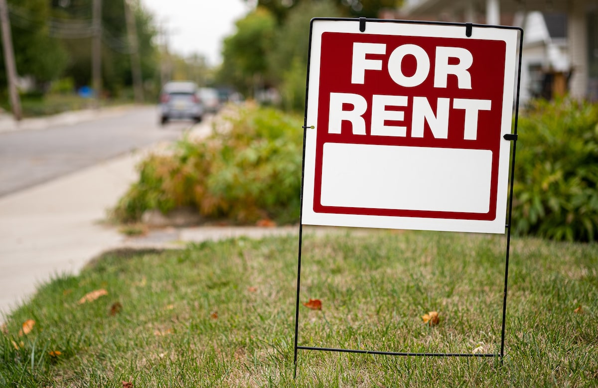 Red and white for-rent sign stuck in residential lawn in the suburbs
