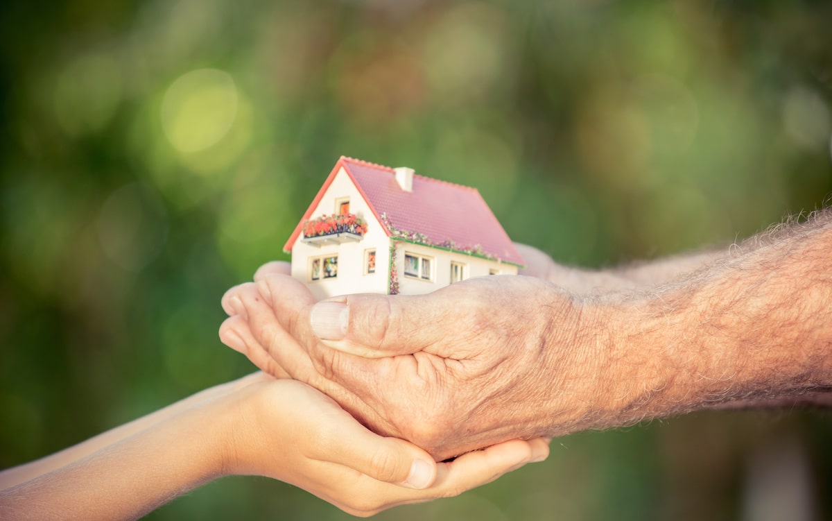 Old and young hands holding multigenerational home model against spring background