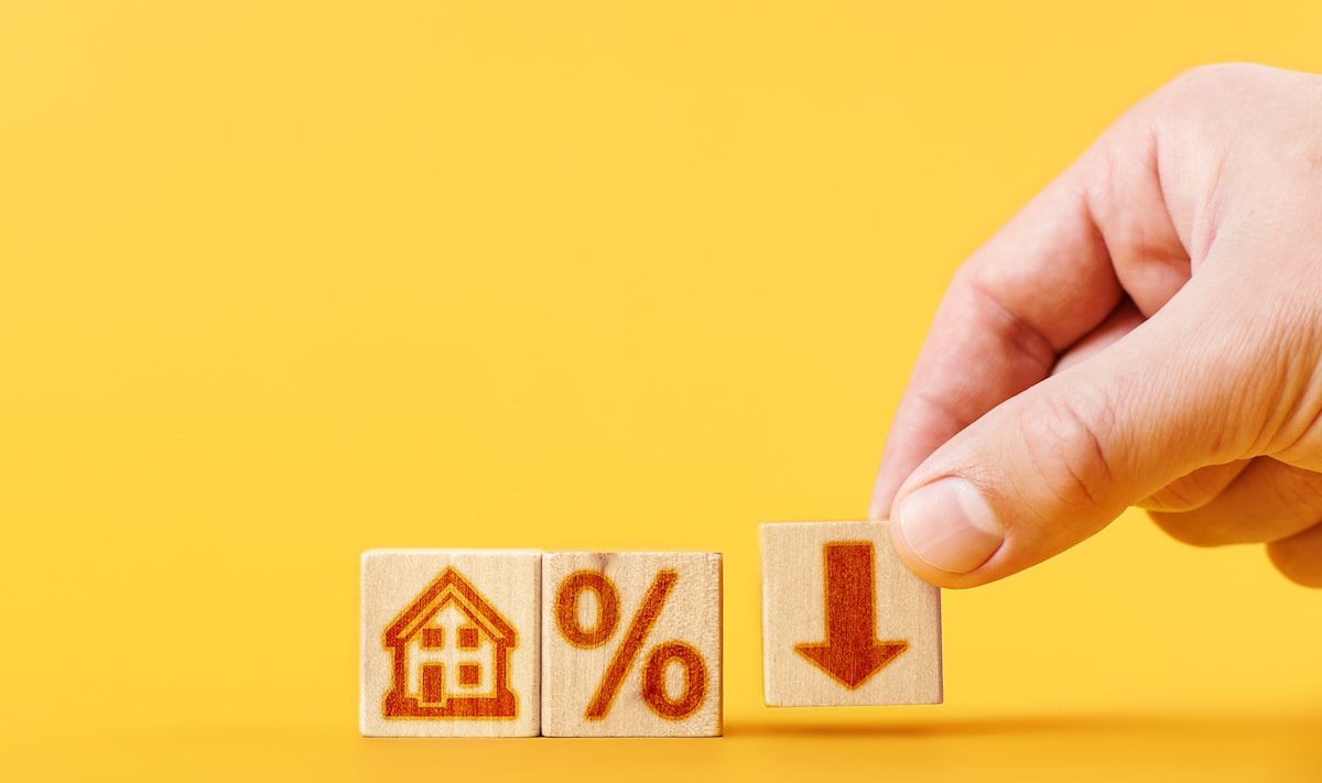 House, percentage, and downward arrow on small wooden blocks against yellow background