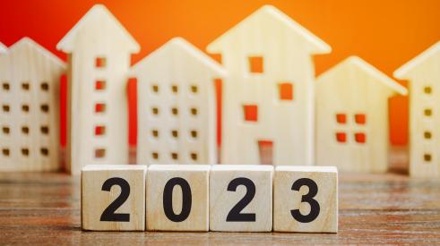 Numbered wooden blocks that say '2023' in front of wooden house models with orange background