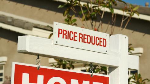 Home for sale sign with 'price reduced' sign at top