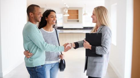 Smiling couple shakes hands with realtor inside a home
