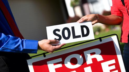 Two people placing sold sign on home for sale sign 