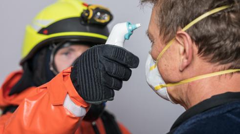 Man in protective gloves measures temperature of man wearing face mask