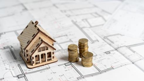 Small house model and stacks of coins on house plans