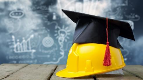 Graduation cap on top of construction hardhat with chalkboard in background