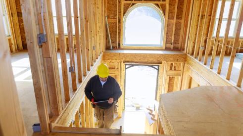 Home builder climbing stairs inside house under construction