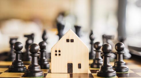 Chess pieces surrounding small wooden house on a chess board