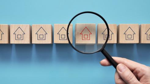 Magnifying glass over wooden block market with house outline