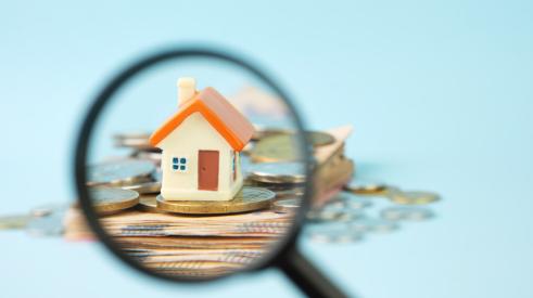 House on coins under magnifying glass