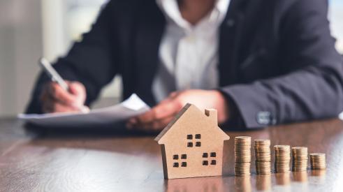 Home model with coin stacks and businessman in background