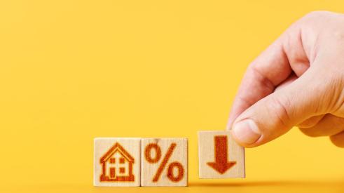 House, percentage, and downward arrow on small wooden blocks against yellow background