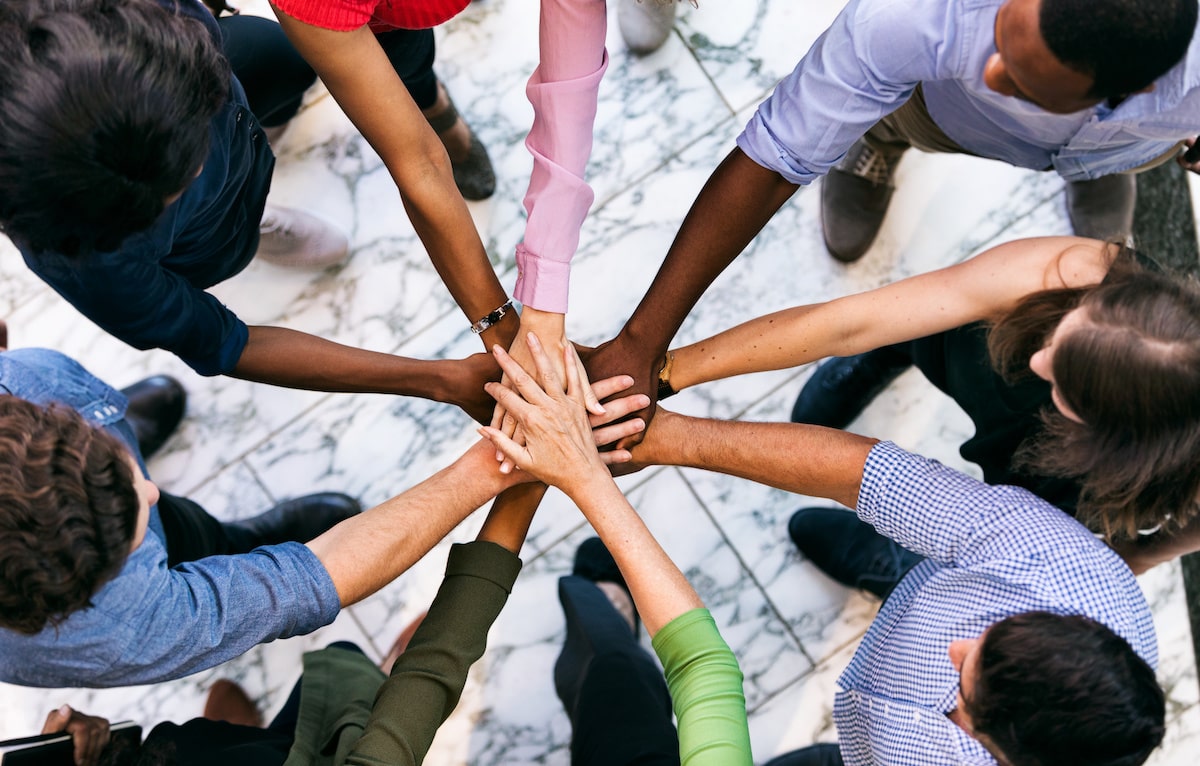 Diverse group of employees stand in circle with hands on top of one another