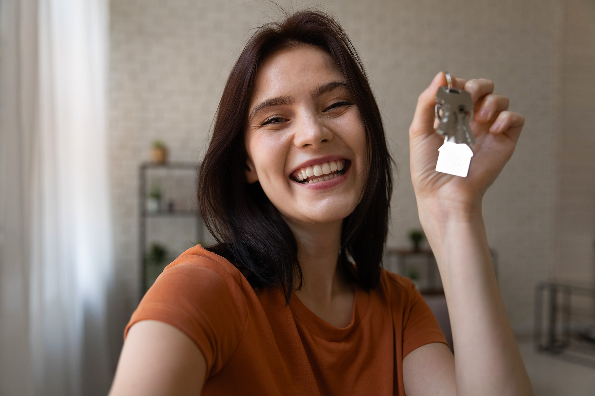 Young female holding keys to new home look at camera shoot selfie portrait