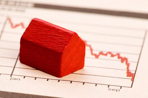 Red house figurine with chart showing home prices dropping