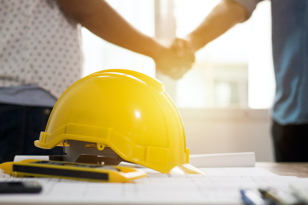 Two people shaking hands with hard hat in foreground