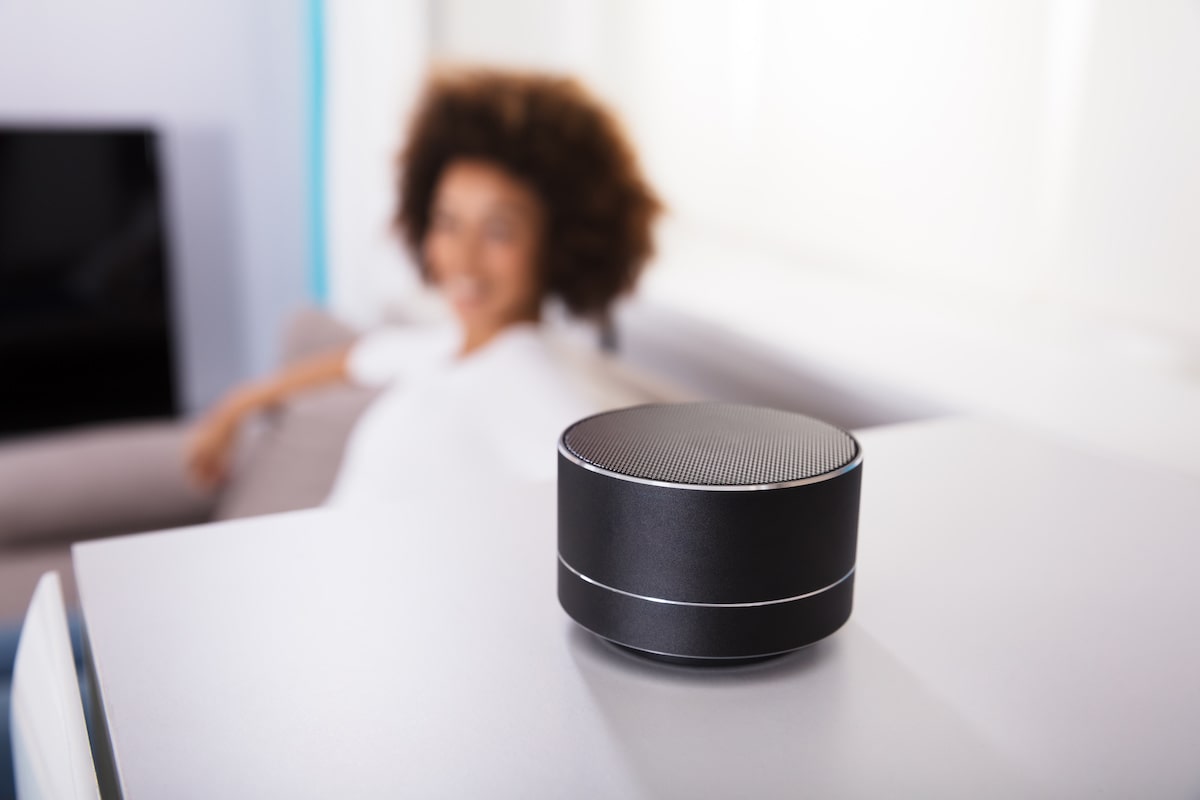 A woman is sitting on the couch, looking at her smart speaker.