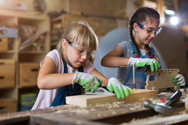 Two girls in a wood workshop planing and sanding their woodworking projects