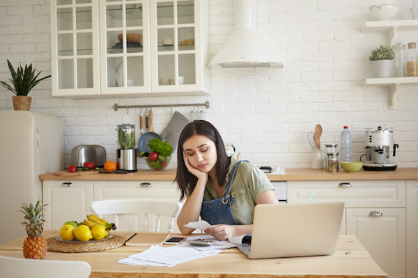 Young woman sitting in kitchen looking sadly at her budget