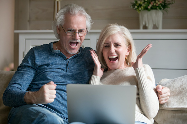 Older couple smiling, cheering to laptop