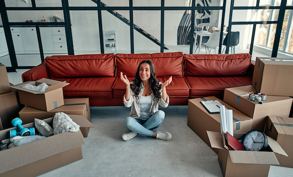 Woman sitting on floor of new house smiling with boxes around 