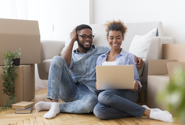 Smiling couple looking at laptop while surrounded by moving boxes