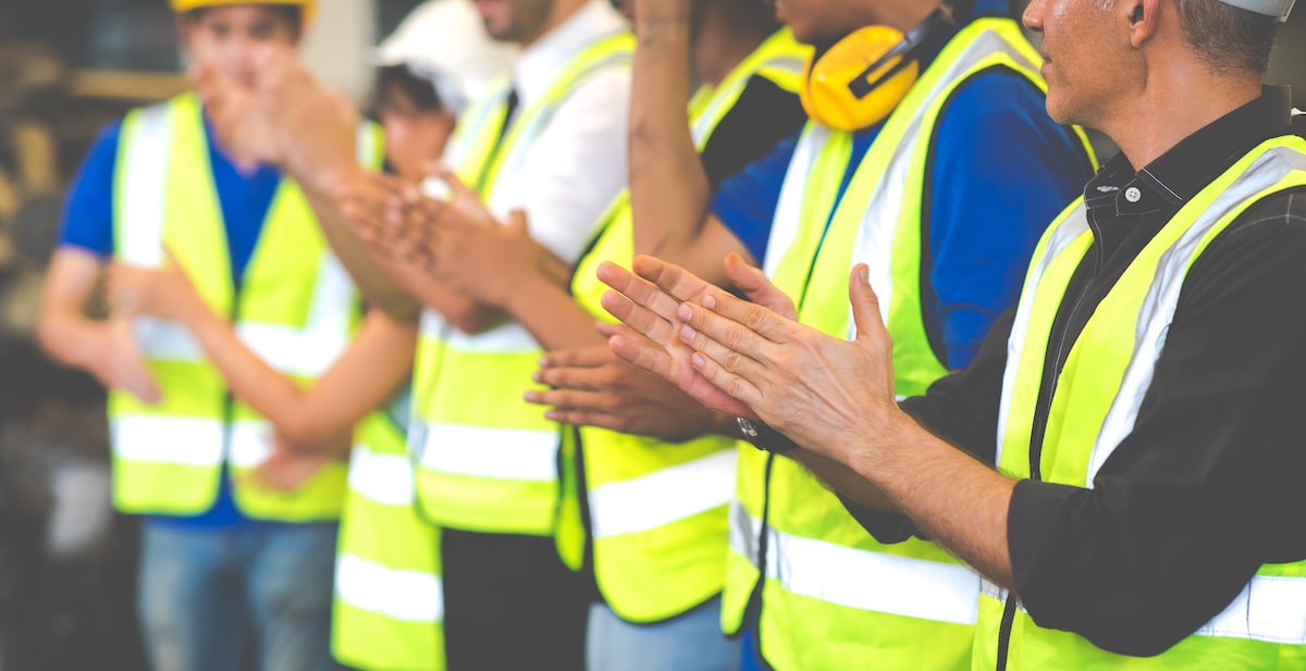 This photo shows a row of construction workers clapping.