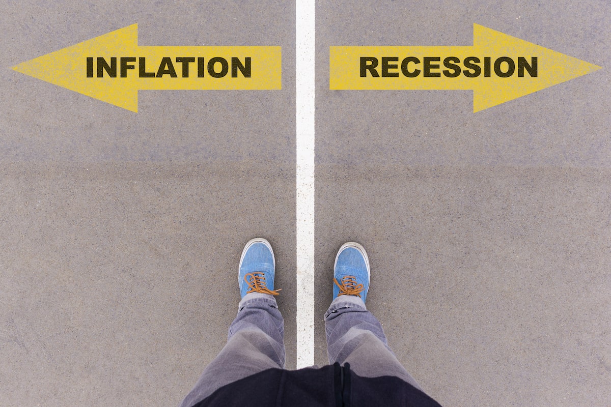 A pair of feet stand on a white line, separating inflation and recession.