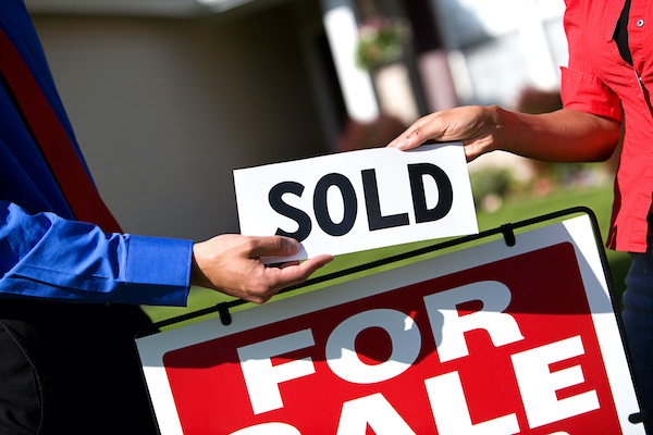 Two people placing sold sign on home for sale sign 