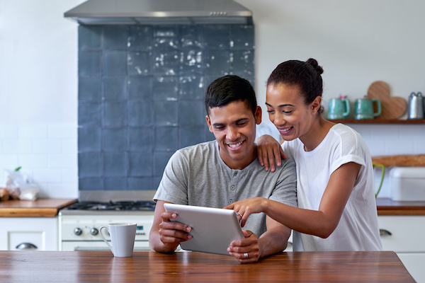 Couple in kitchen smiling together while looking at tablet