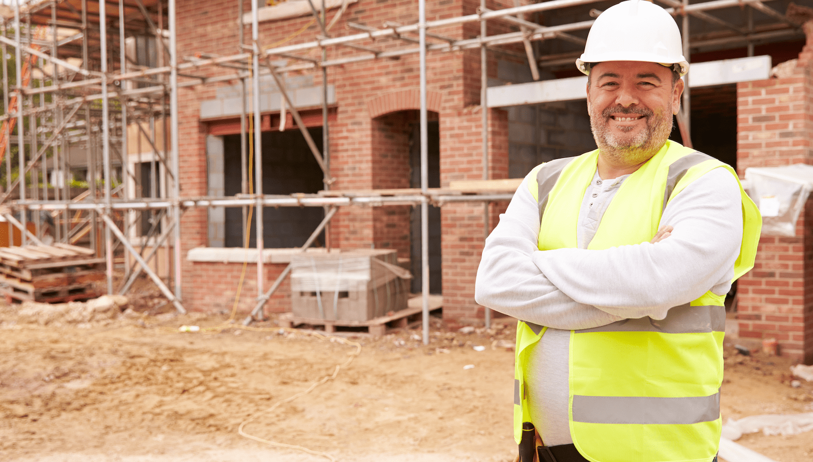 Happy home builder who enjoys his work standing in front of brick home under construction