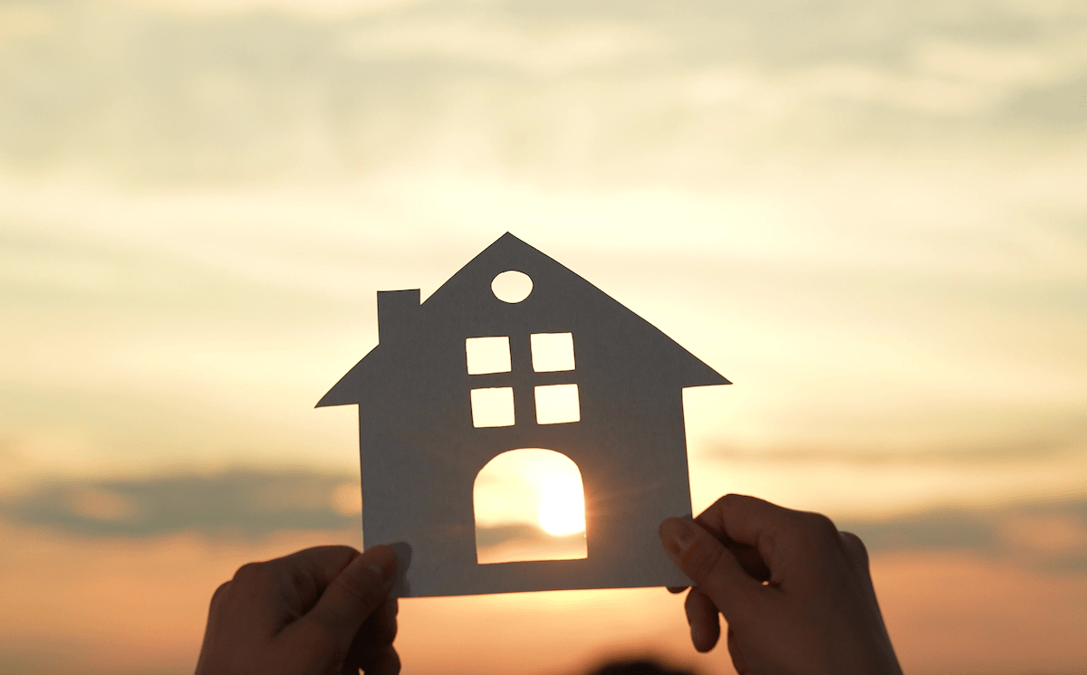 Hands holding up paper cutout of house with sun shining through