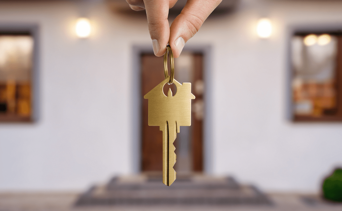 Hand holding house key in front of new home