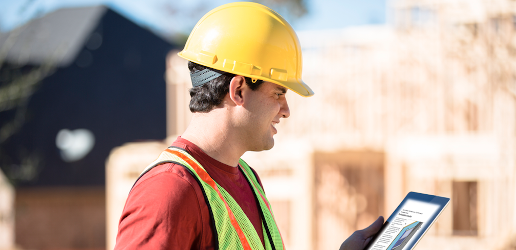 Construction worker wearing hard hat and looking at tablet with specifications on building jobsite
