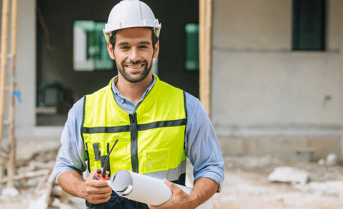 Smiling home builder holding a rolled set of house plans under his arm