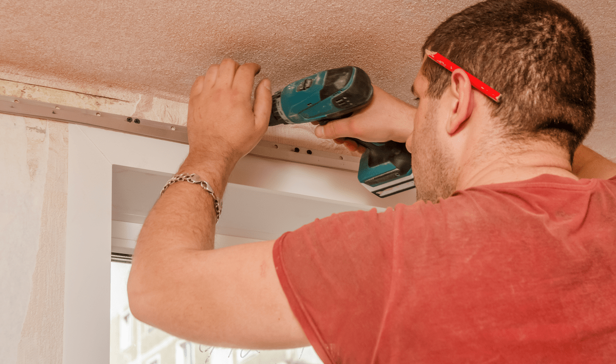 Young man using power drill installing drywall