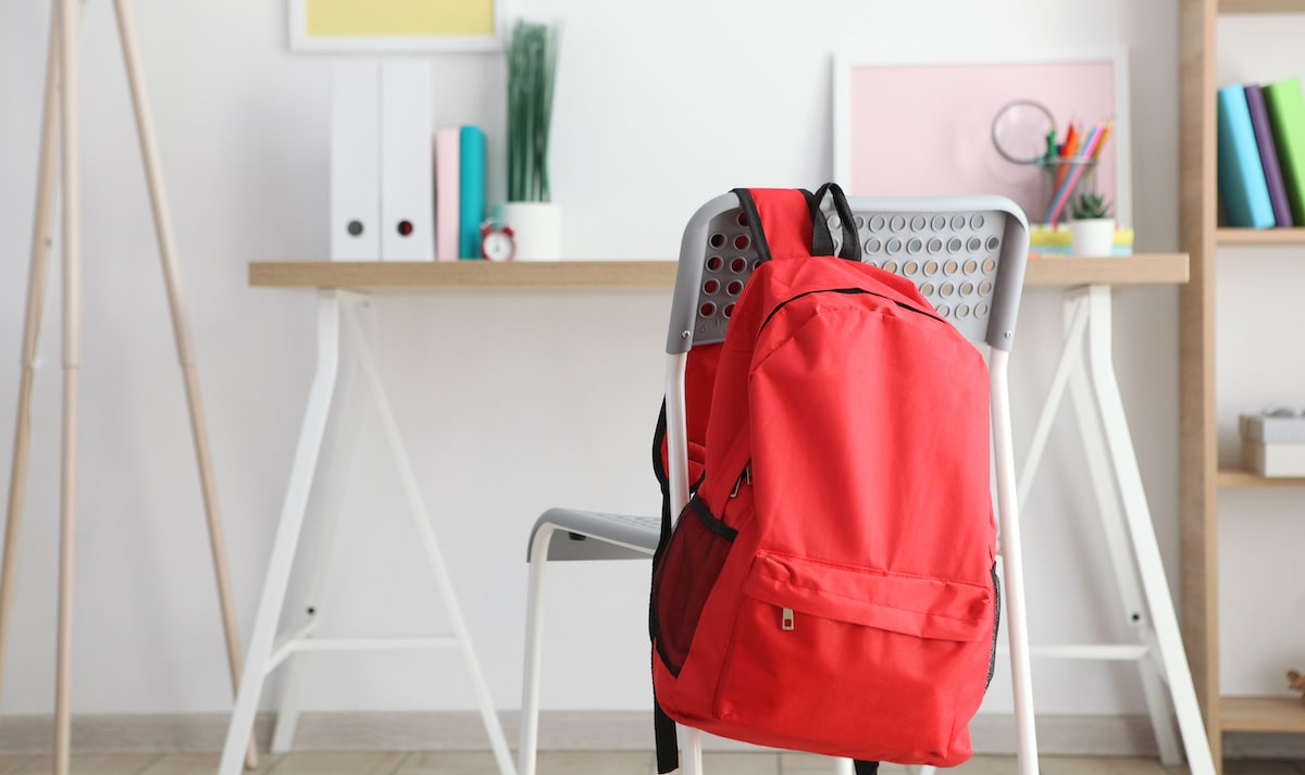 Red backpack hanging on chair in bright home workspace