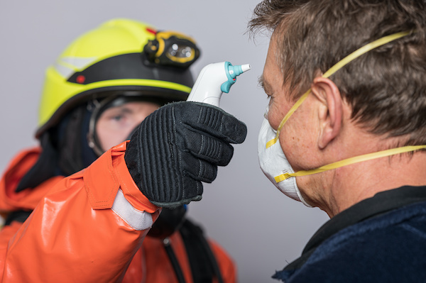 Man in protective gloves measures temperature of man wearing face mask
