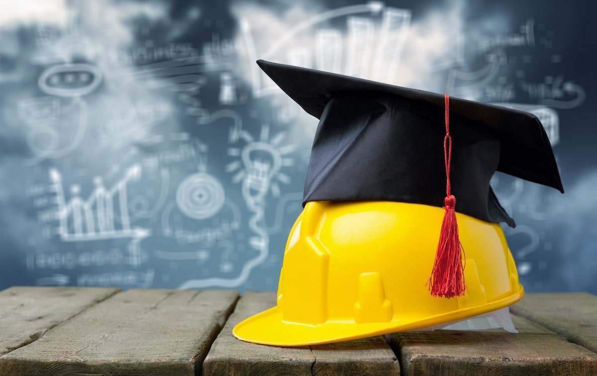 Graduation cap on top of construction hardhat with chalkboard in background