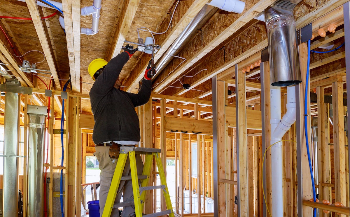 Home builder standing on ladder installing downlight in wood-framed ceiling 