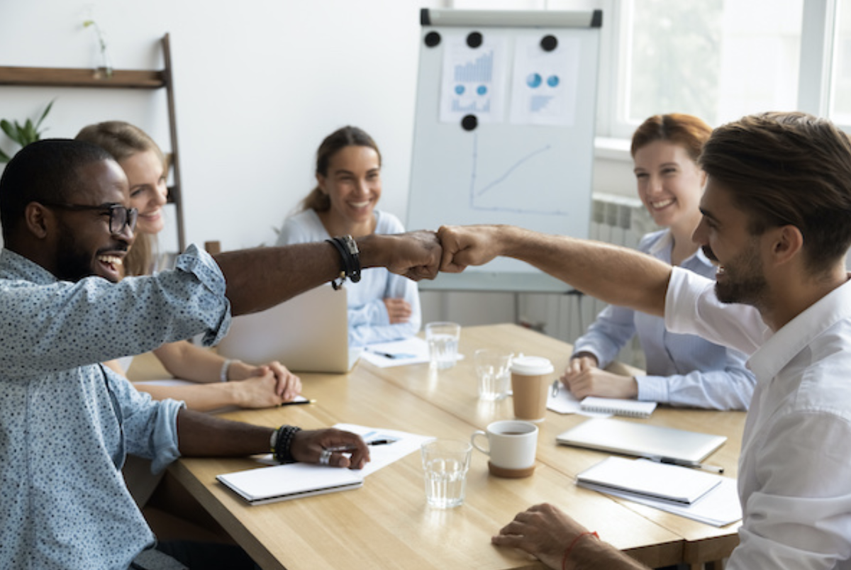 Coworkers fist bumping at a conference table show teamwork and positive company culture