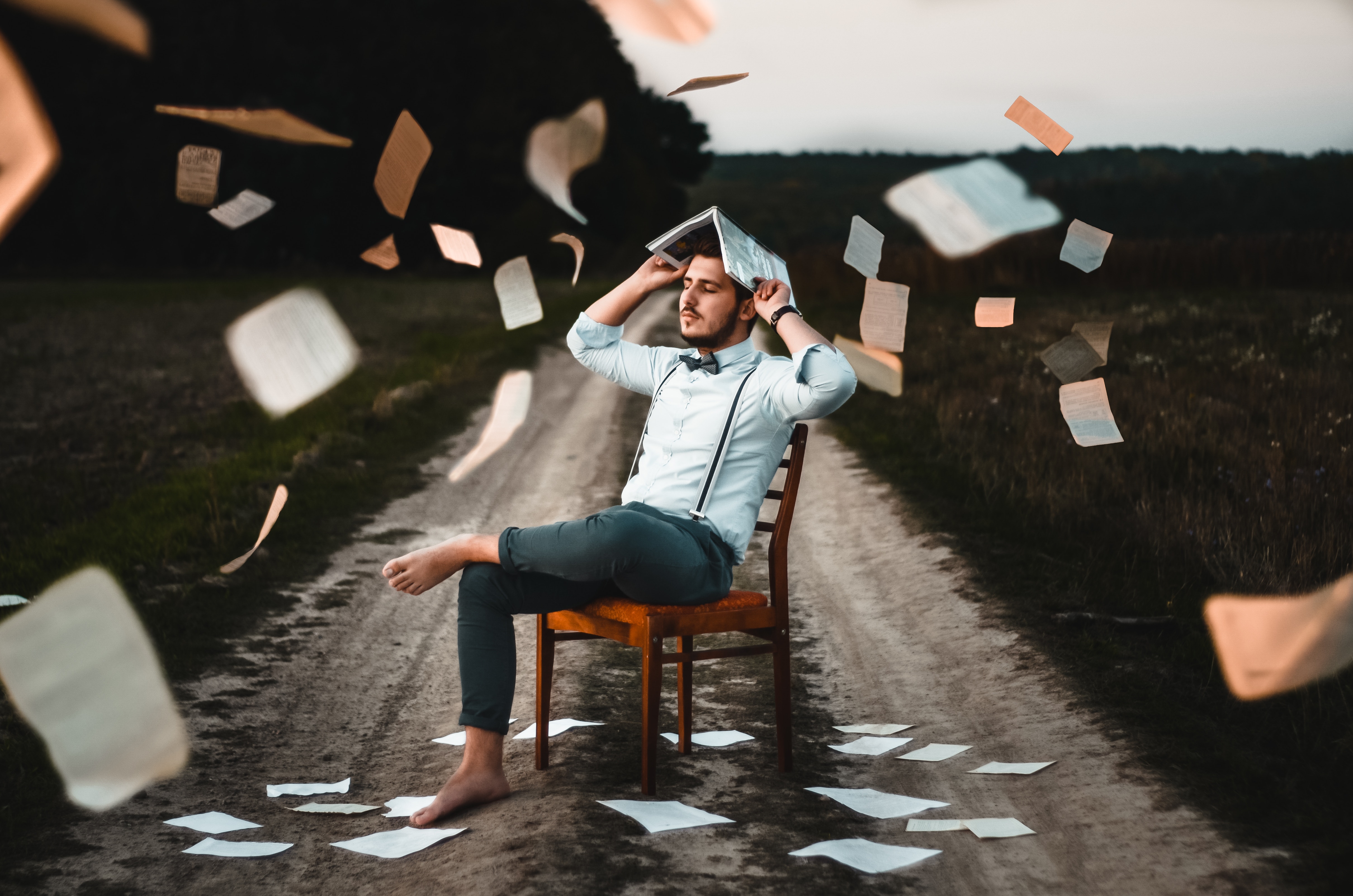 man sitting on chair on road with papers flying everywhere