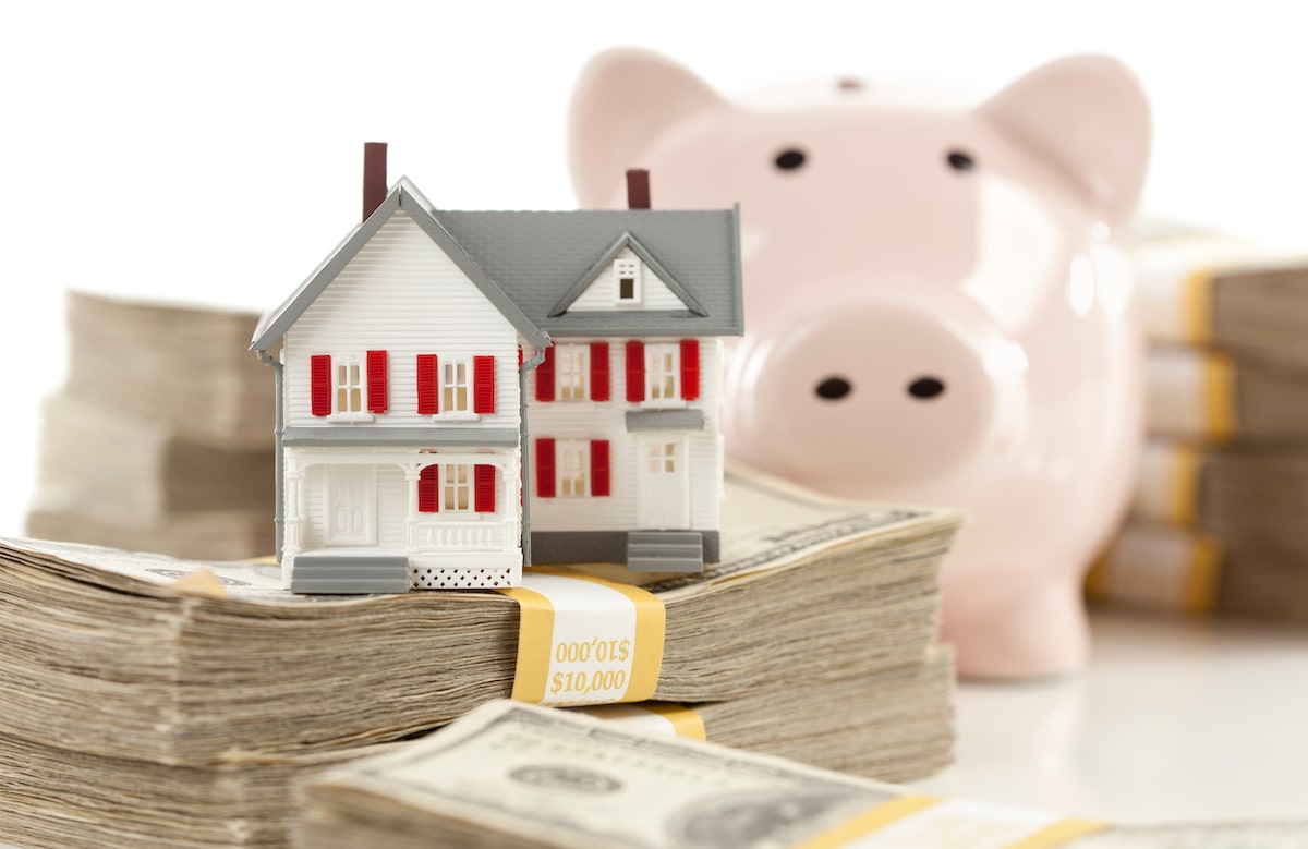 House stacked on money in front of piggy bank
