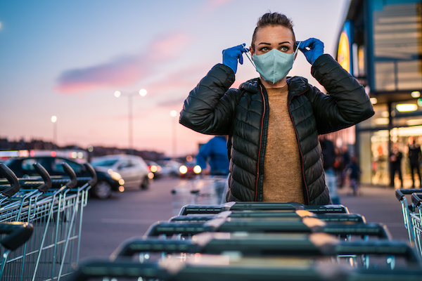 woman wearing protective face mask and latex gloves with shopping carts in carpark outside grocery store 