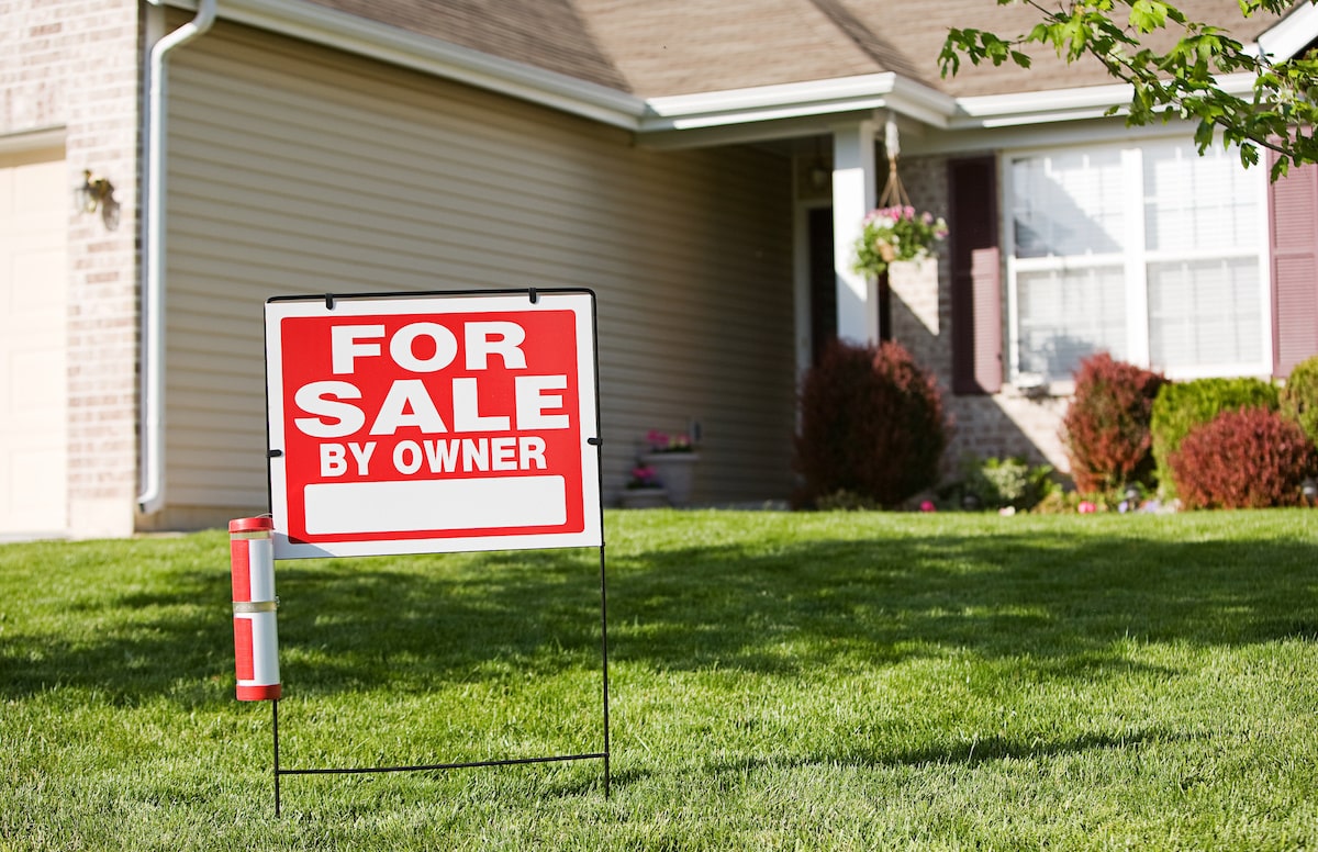 Red and white 'for sale by owner' sign outside of residential home